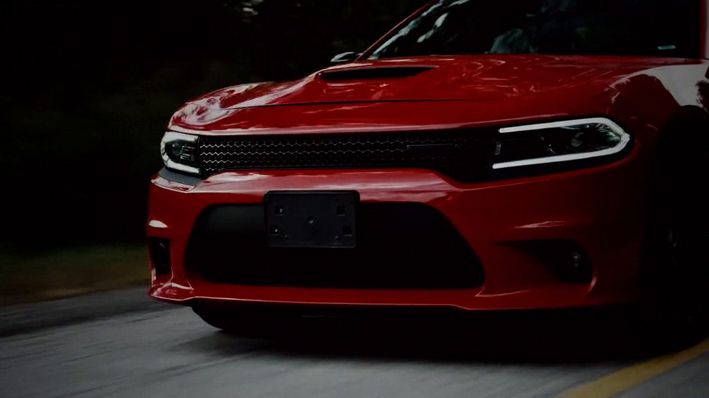 Red Dodge Charger driving on a tree-lined road, front view